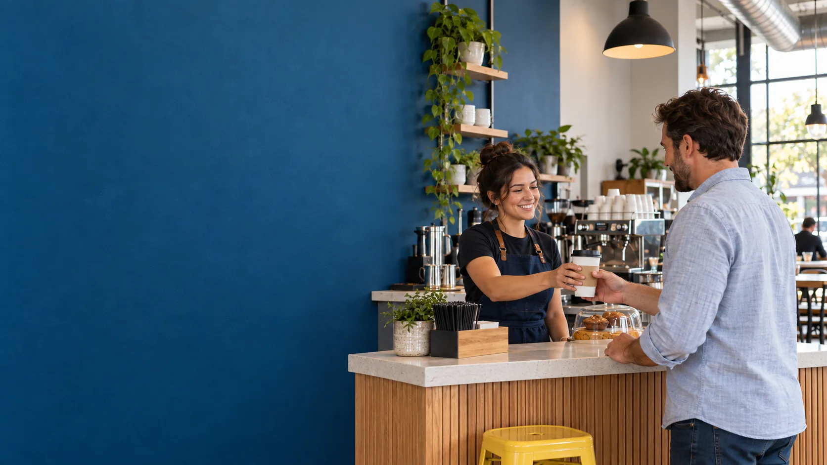 A barista serving a customer at the counter of a bright, blue-walled café.